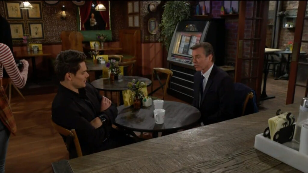 Adam Newman and Jack Abbott talk while at a table in the coffee shop. Adam's arms are crossed. - Young and The Restless recap for Jan 2, 2023
