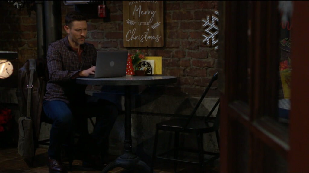 Daniel sits alone in the coffee shop, typing on his laptop