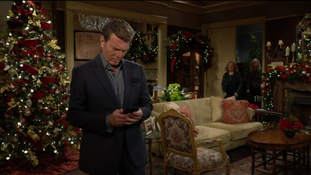 Jack looks pensively at his cellphone in front of the tree, while Ashley and Traci come into the living room