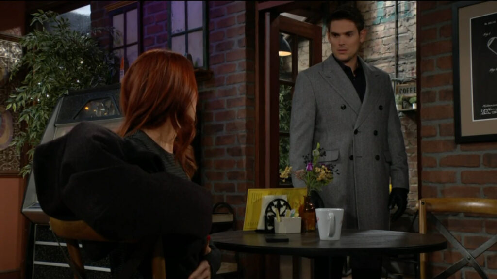 Adam stands in the doorway of the coffee shop and talks to Sally, who's sitting at a table