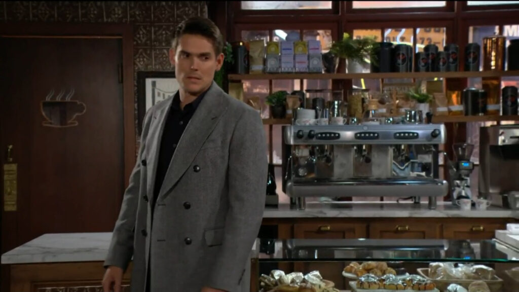 Adam gets up from the table and stands near the counter in the coffee shop