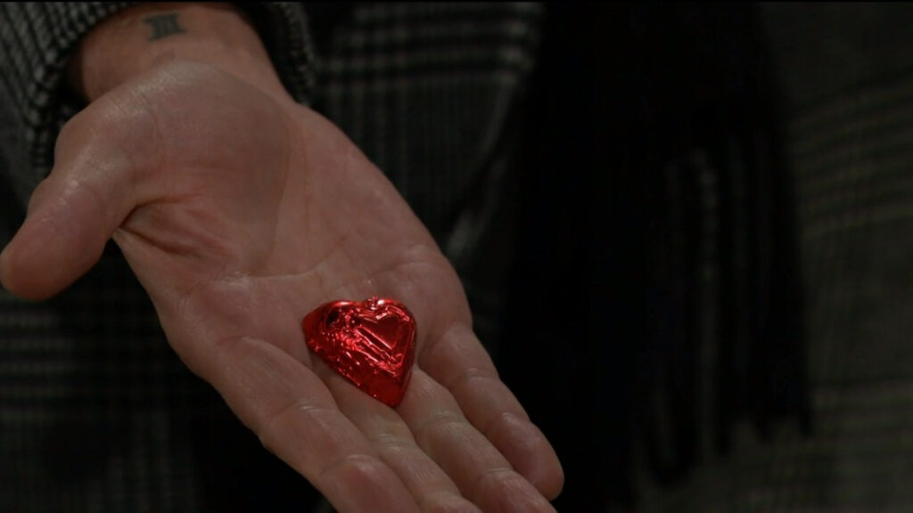 A red, foil-wrapped chocolate heart rests in Billy's open hand