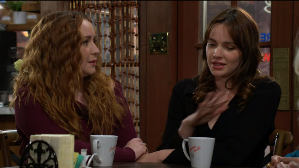 Mariah and Tessa sit at a table with coffee mugs in front of them, talking