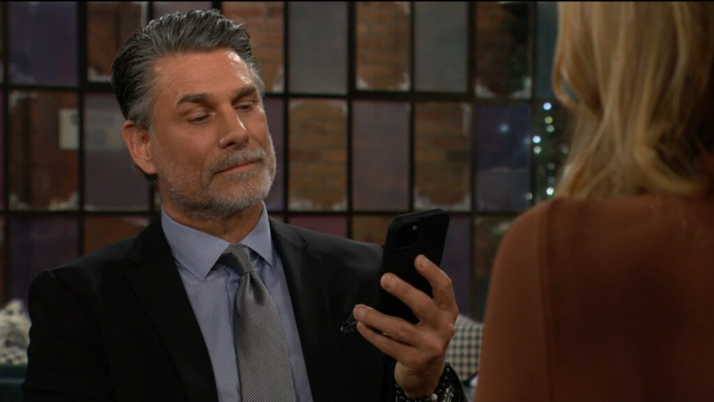 Jeremy looks at his phone as he sits at the table with Phyllis
