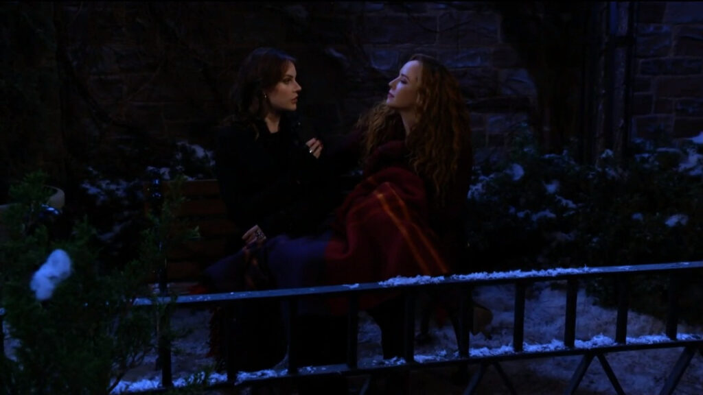 Mariah and Tessa sit on a park bench with a blanket as they talk
