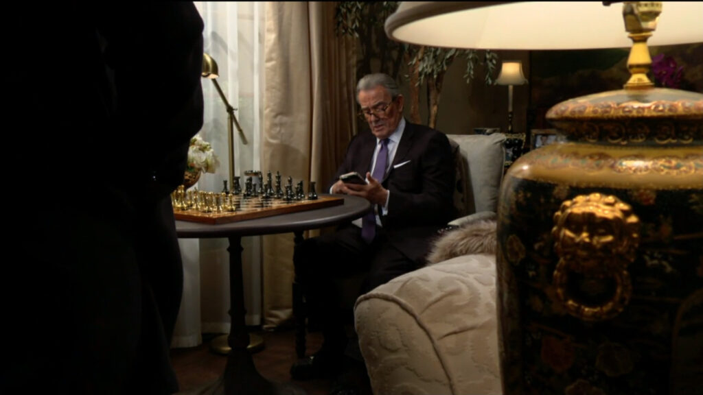Victor sits in front of a chessboard, looking at his phone, when Adam walks in