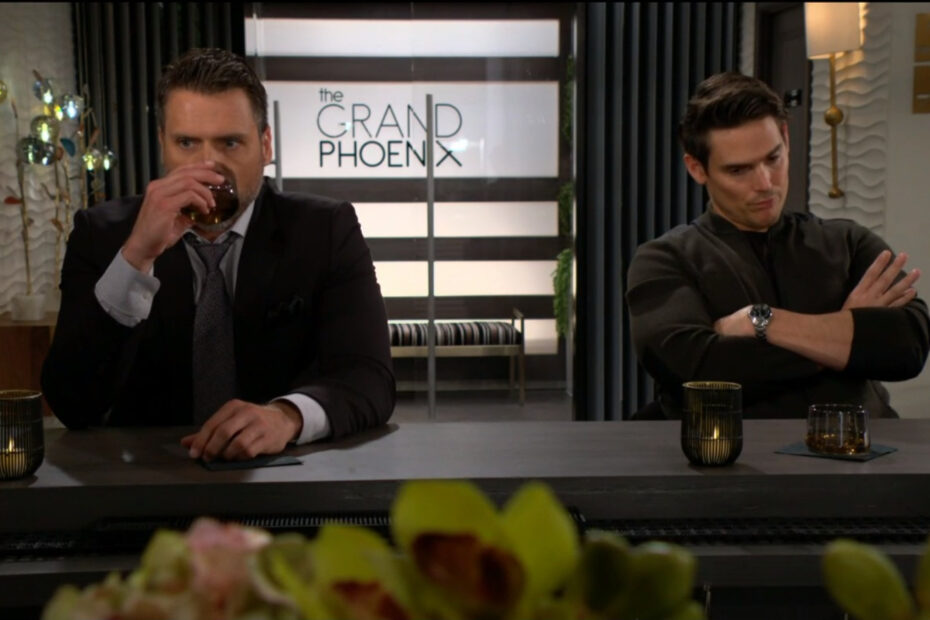 Nick and Adam sit at the bar in the hotel lobby and talk. Adam's arms are crossed while Nick takes a drink.