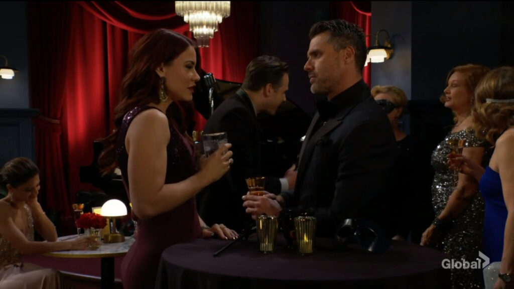 Nick and Sally stand at a table with a drink in hand as they talk