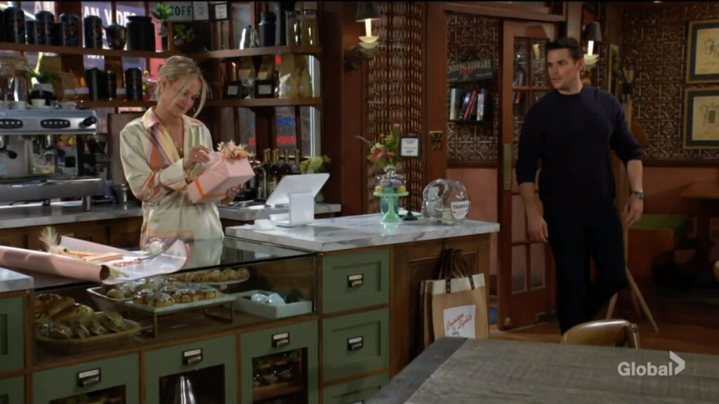 Adam comes into the coffee shop and sees Sharon wrapping a gift