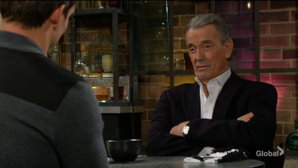 Victor sits with his arms crossed as he talks with Adam.
