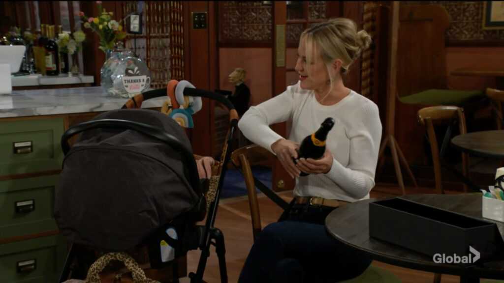 Sharon holds the bottle of champagne as she talks to Aria. Someone is looking stealthily through the door.