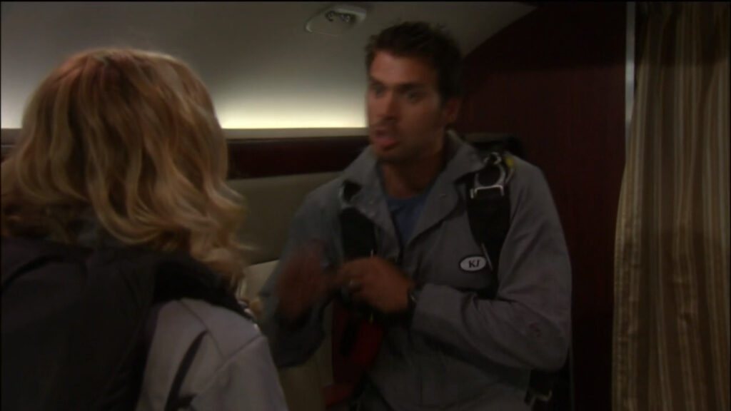 Nick talks to Sharon in the airplane. They're both wearing parachutes.