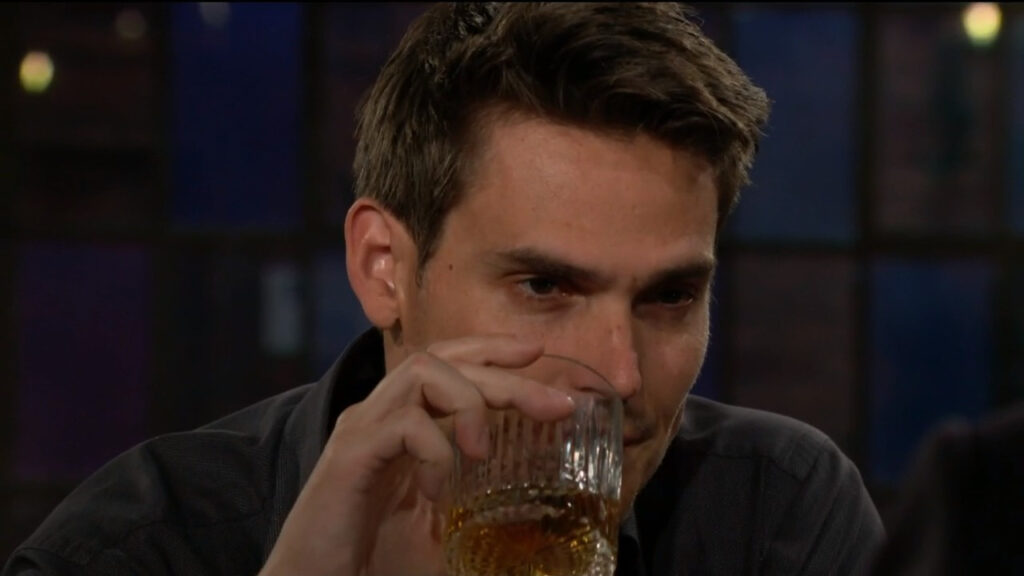 Adam holds his drink as he talks with Victor.