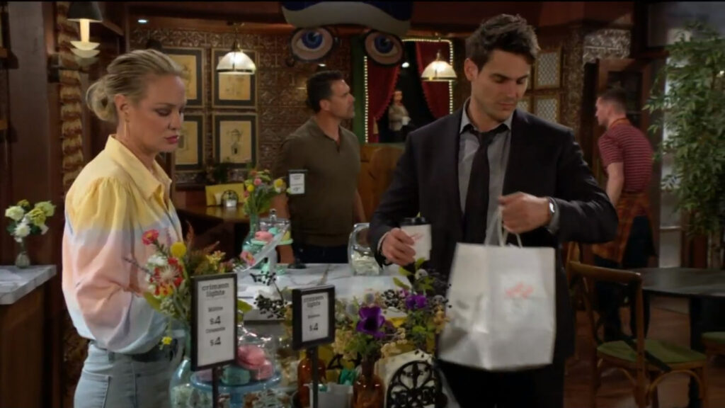 Adam takes a bag of takeout and a cup of coffee from Sharon as Nick walks in.