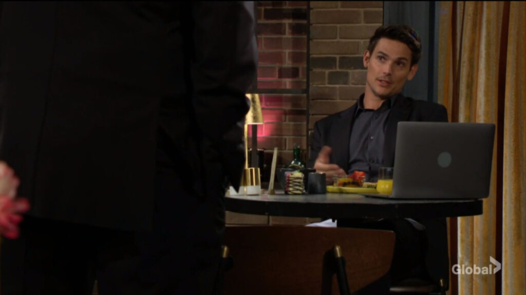 Adam sits at a table and talks to Victor.