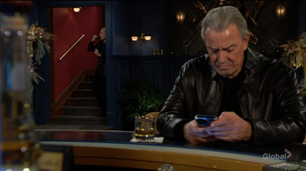 Victor sits at the bar while Nikki drinks behind him.