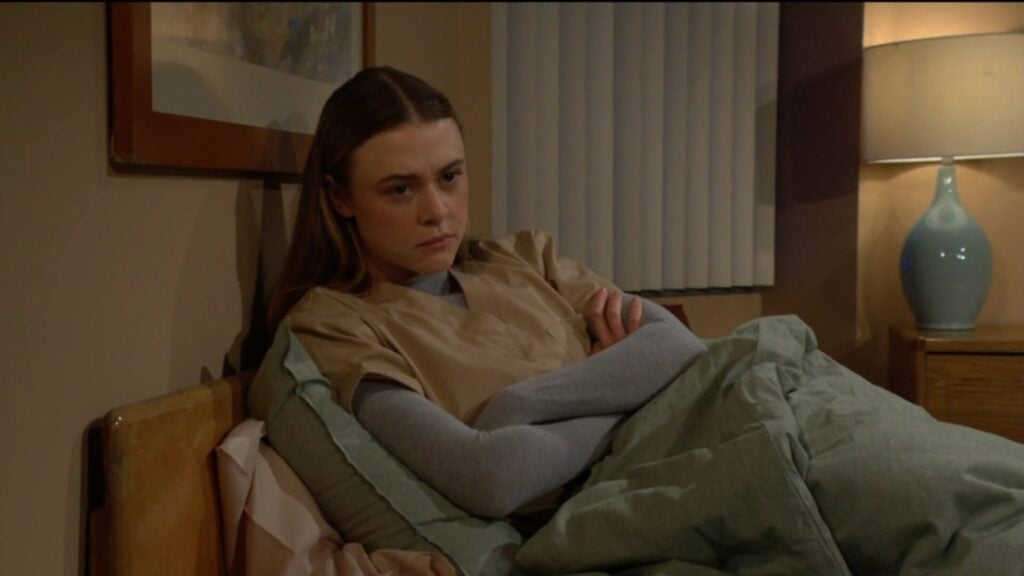 Claire sits in bed with her arms crossed.